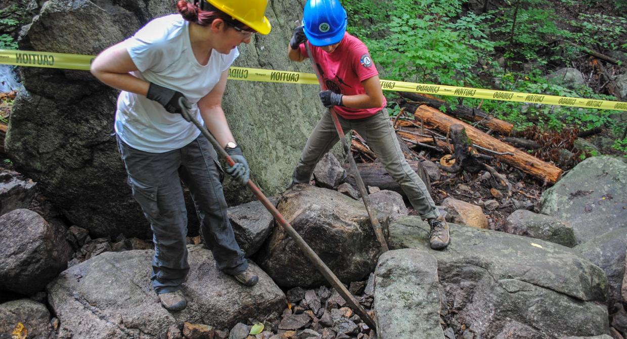 A trail volunteer and an Conservation Corps service member using rock bars to move a rock. Photo by Heather Darley.